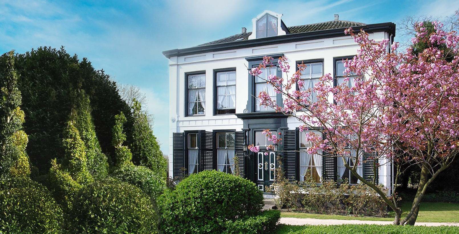 Het witte Huis Grol van voren, met donkere luiken en een bloesemboom